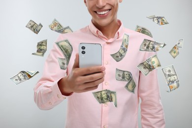 Image of Man using smartphone on light background, closeup. Money flying around device