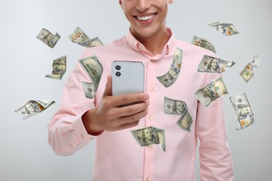 Man using smartphone on light background, closeup. Money flying around device