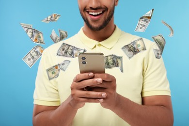 Image of Man using smartphone on light blue background, closeup. Money flying around device
