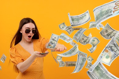 Excited woman throwing money on orange background. Dollar bills flying away from her