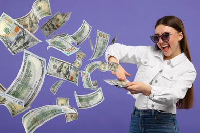 Happy woman throwing money on dark violet background. Dollar bills flying away from her