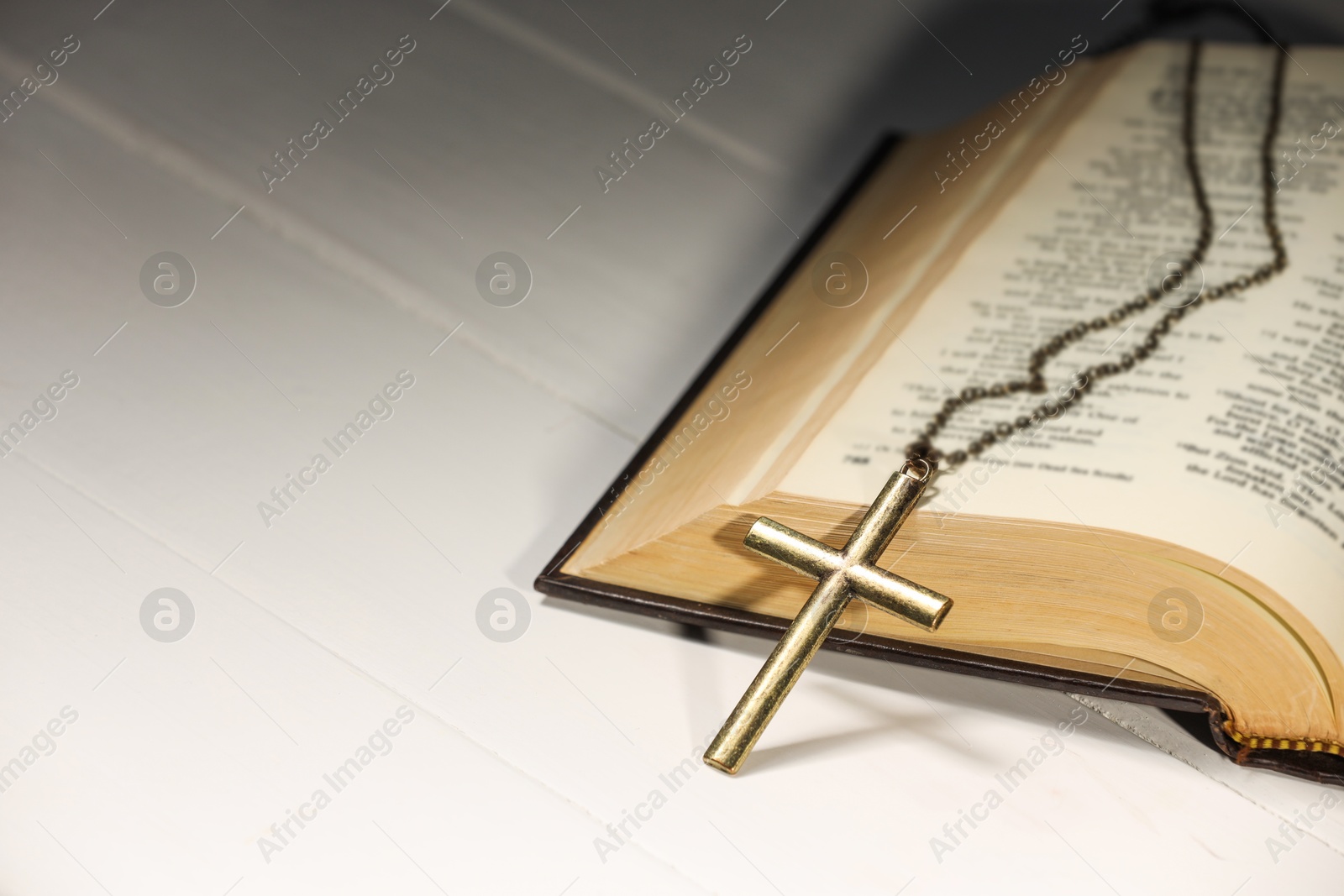 Photo of Cross with chain and Bible on white wooden table, closeup with space for text. Religion of Christianity