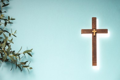 Photo of Shining cross and eucalyptus branches on turquoise background, space for text. Religion of Christianity