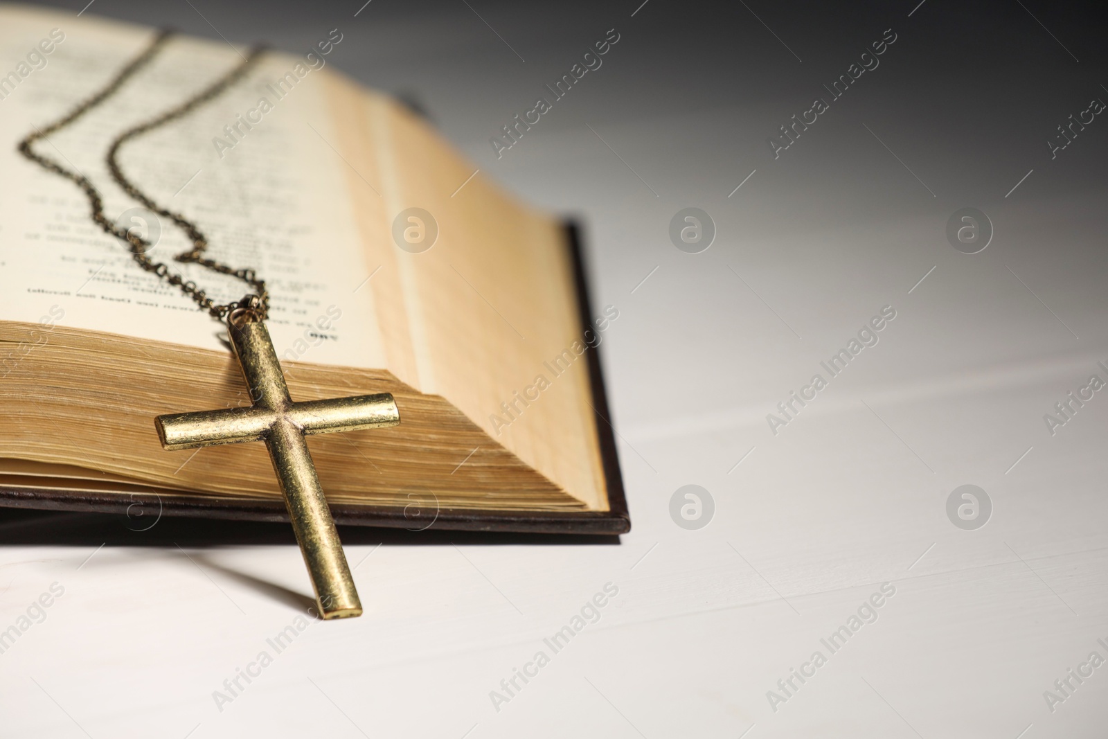 Photo of Cross with chain and Bible on white wooden table, closeup with space for text. Religion of Christianity