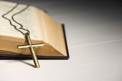 Cross with chain and Bible on white wooden table, closeup with space for text. Religion of Christianity