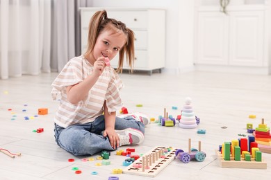 Photo of Cute little girl playing with math game Fishing for Numbers on floor indoors