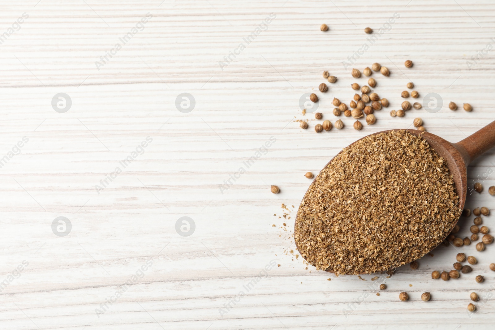 Photo of Coriander powder in spoon and seeds on wooden table, top view. Space for text