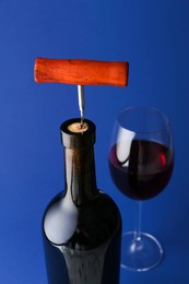 Photo of Bottle with corkscrew and glass of wine on blue background, closeup