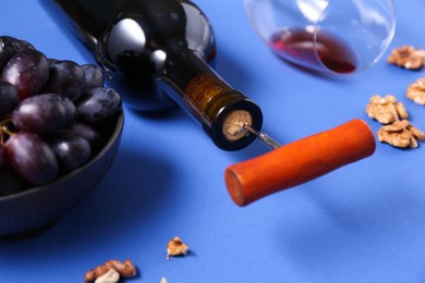 Bottle with corkscrew, grapes and walnuts on blue background, closeup