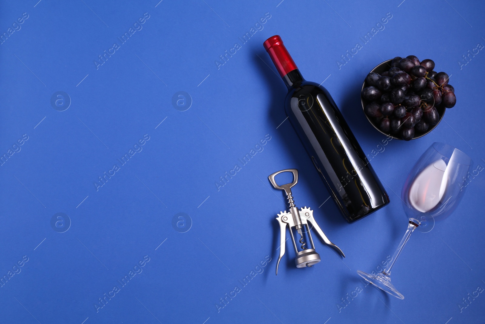 Photo of Wing corkscrew, wine, grapes and glass on blue background, flat lay. Space for text