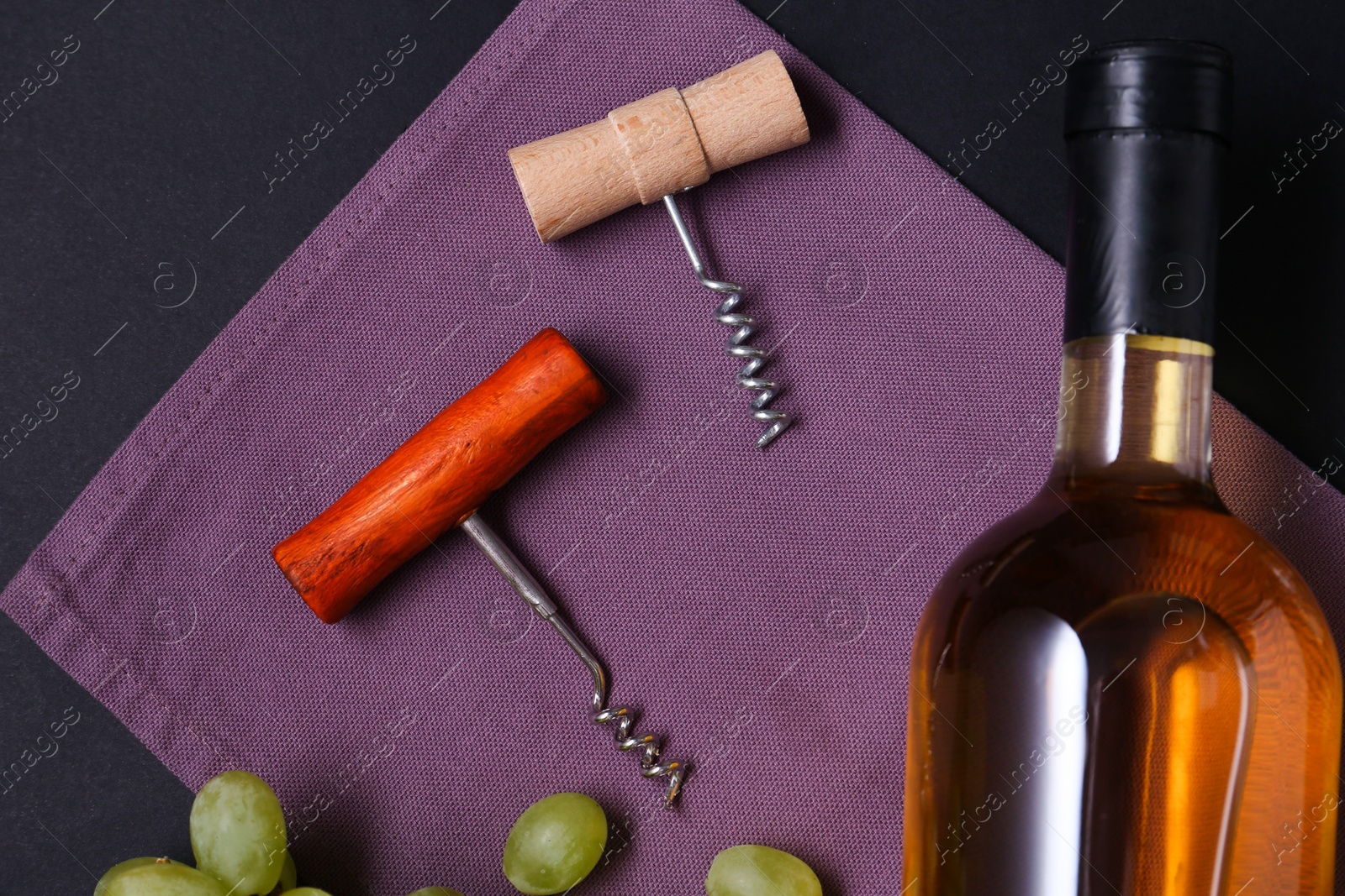 Photo of Corkscrews, wine and grapes on black background, flat lay