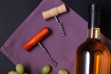 Photo of Corkscrews, wine and grapes on black background, flat lay