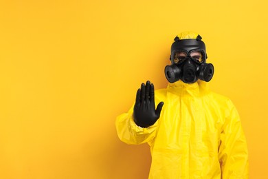 Photo of Worker in gas mask showing stop gesture on yellow background. Space for text