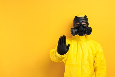 Worker in gas mask showing stop gesture on yellow background. Space for text