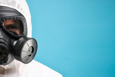 Worker in gas mask on light blue background, closeup. Space for text