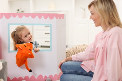 Photo of Puppet theatre. Girl performing show with toy to her smiling mother at home