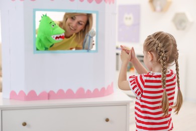 Photo of Puppet theatre. Smiling mother performing show with toys to her daughter at home, selective focus