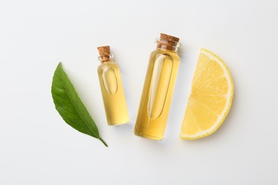 Photo of Bottles of essential oils, lemon and green leaf on white background, flat lay