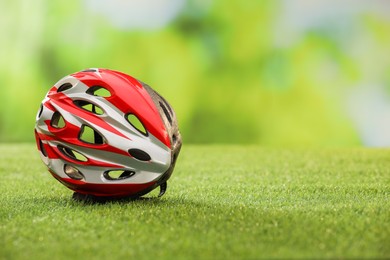 Colorful protective helmet on green grass, space for text