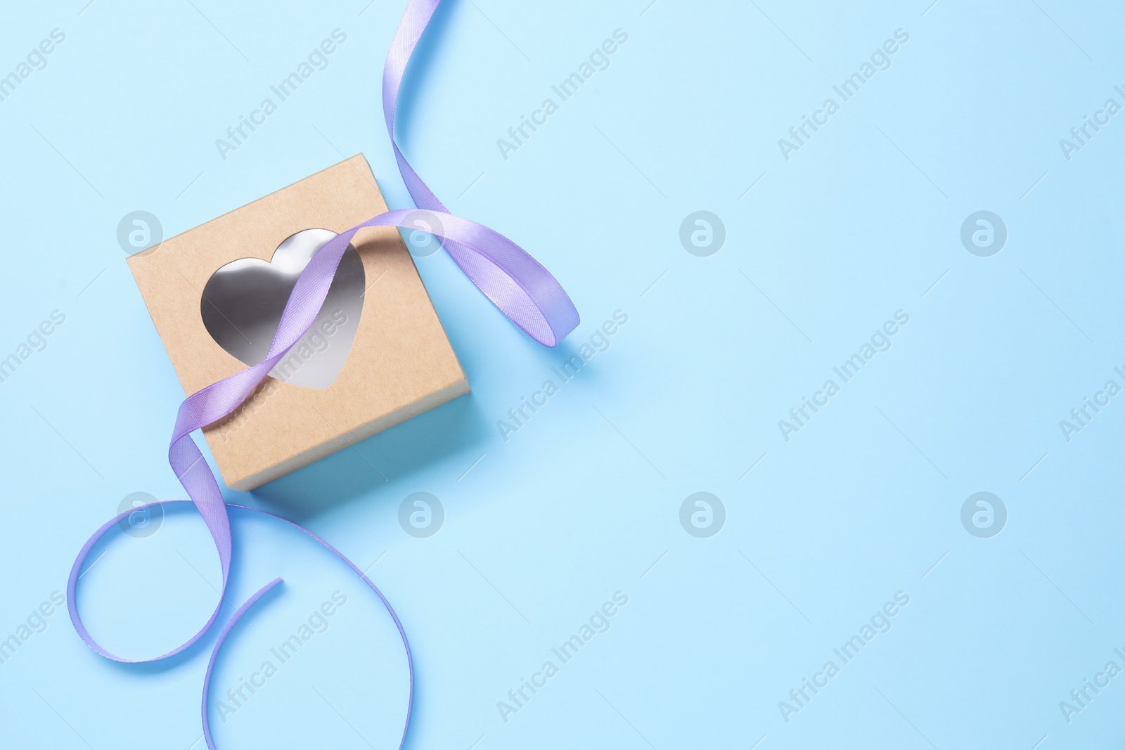 Photo of Beautiful violet ribbon and gift box with heart on light blue background, flat lay. Space for text