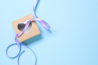 Photo of Beautiful violet ribbon and gift box with heart on light blue background, flat lay. Space for text