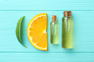 Bottles of essential oils, orange and green leaf on turquoise wooden table, flat lay