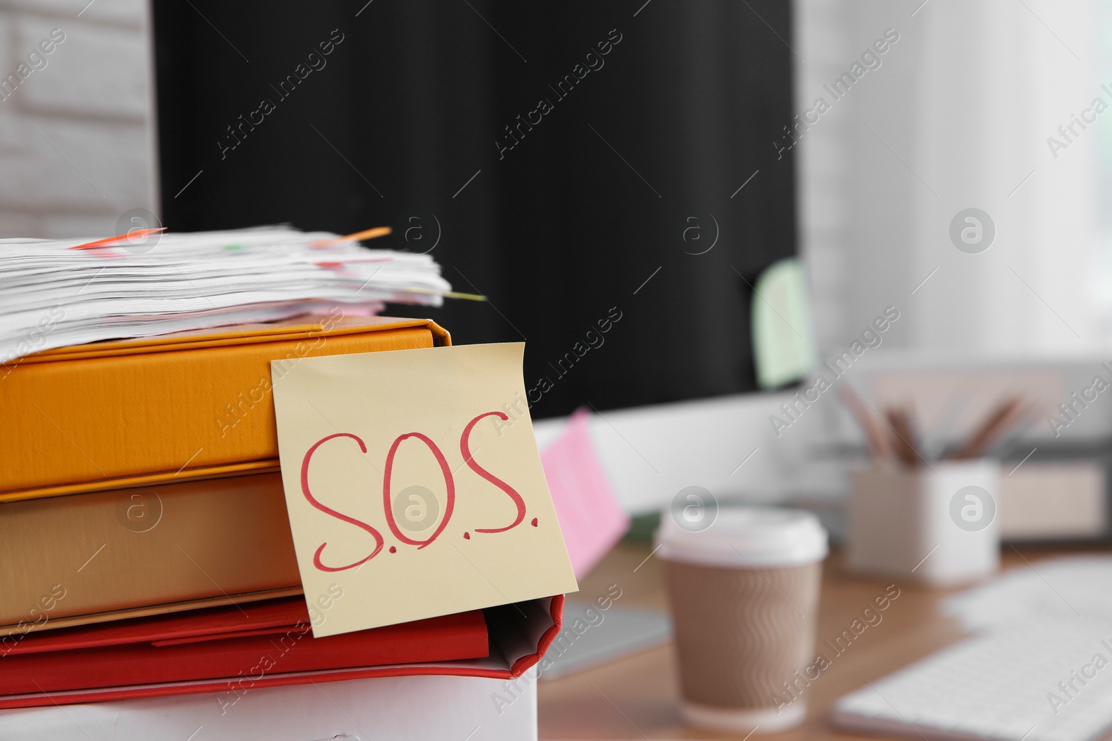 Photo of Note with word SOS and stationery on wooden table at workplace, closeup