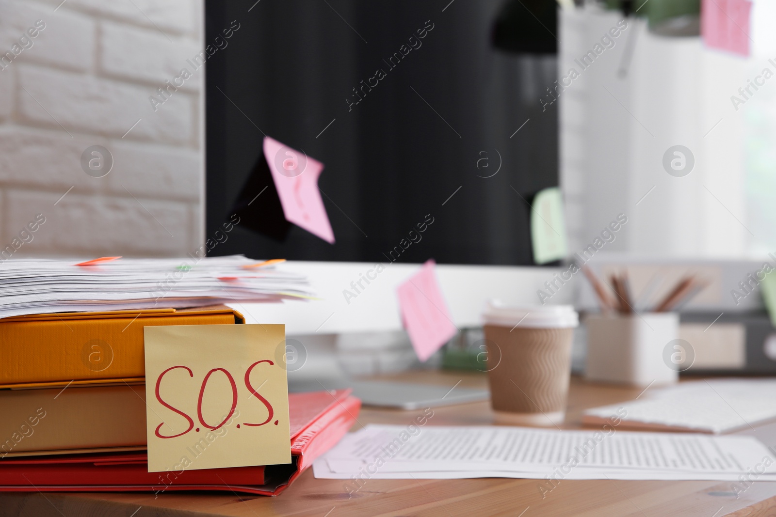 Photo of Note with word SOS and stationery on wooden table at workplace