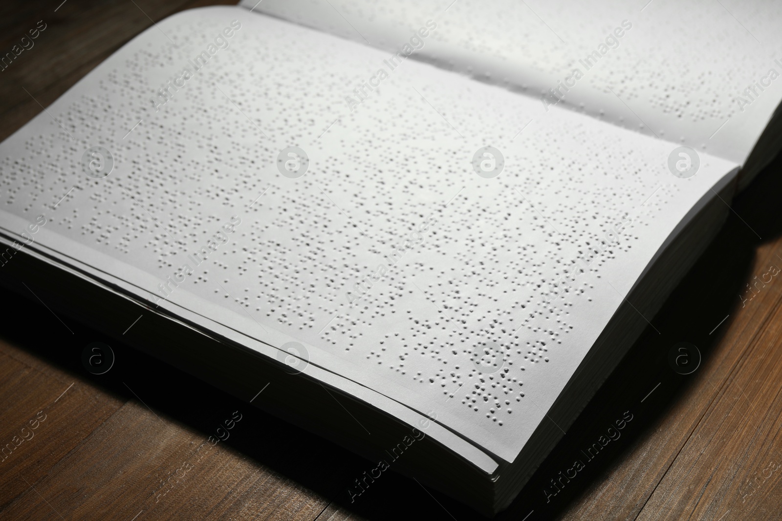 Photo of Book with Braille text on wooden table, closeup. Education and leisure for blind people