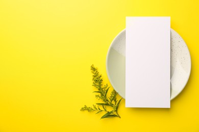 Photo of Empty menu, plate and floral decor on yellow background, top view. Mockup for design