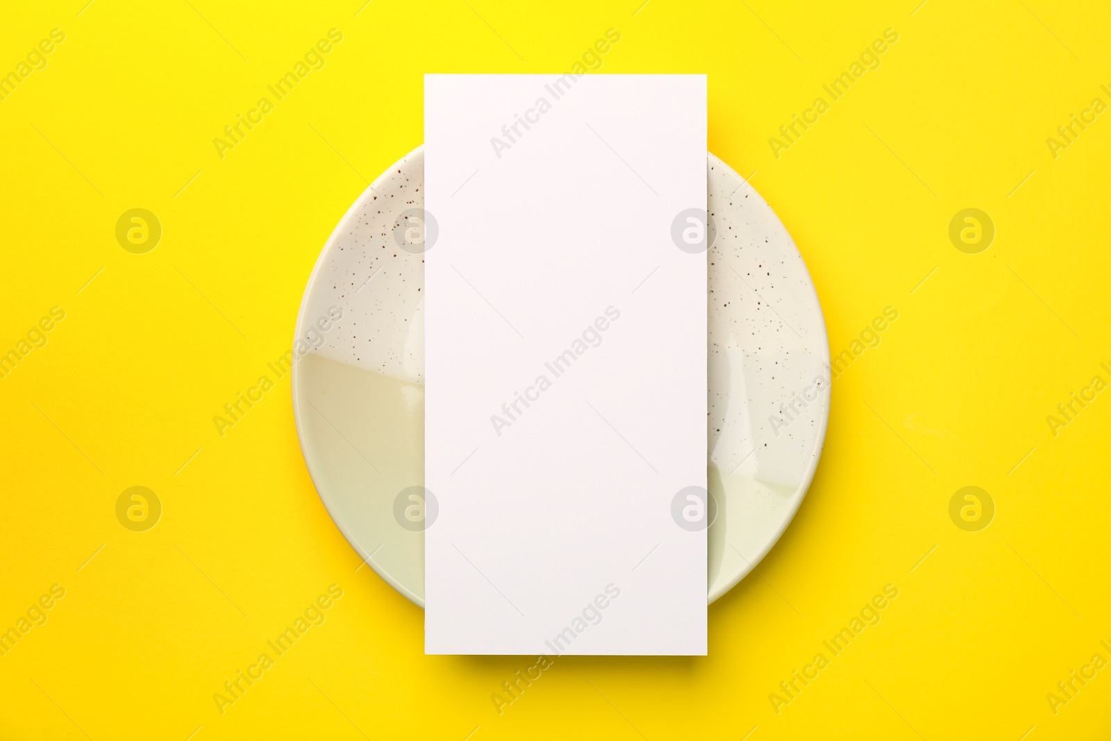 Photo of Empty menu and plate on yellow background, top view. Mockup for design