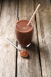 Photo of Delicious protein shake in glass and spoon with powder on wooden table