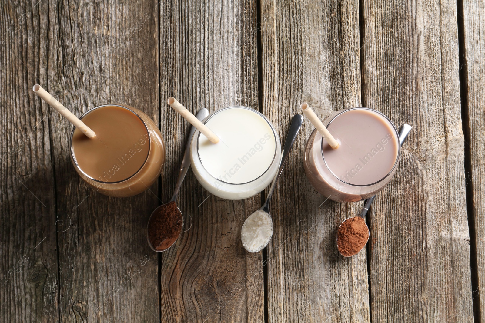 Photo of Delicious protein shakes in glasses and spoons with powder on wooden table, flat lay