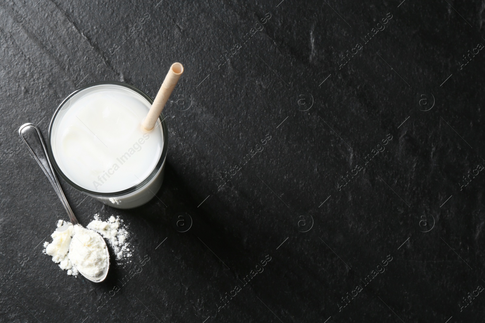 Photo of Delicious protein shake in glass and spoon with powder on black table, top view. Space for text