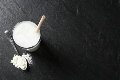 Photo of Delicious protein shake in glass and spoon with powder on black table, top view. Space for text