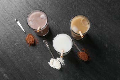 Photo of Delicious protein shakes in glasses and spoons with powder on black table, flat lay