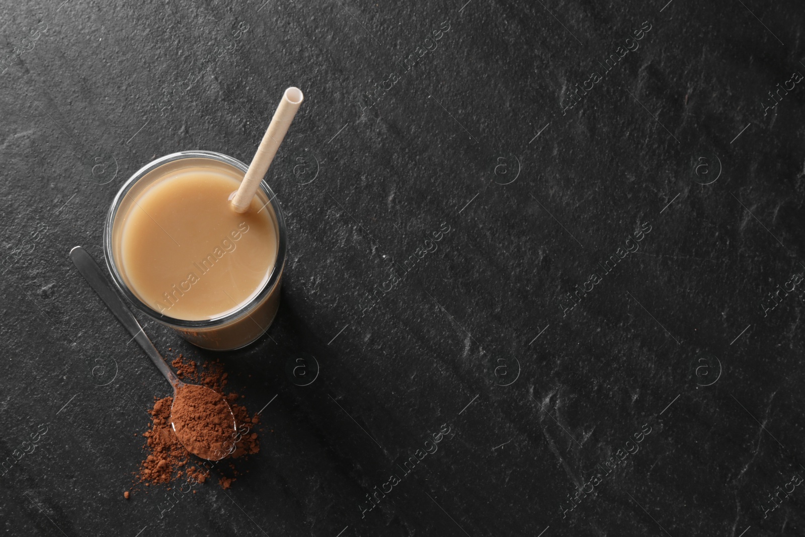 Photo of Delicious protein shake in glass and spoon with powder on black table, top view. Space for text