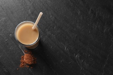 Photo of Delicious protein shake in glass and spoon with powder on black table, top view. Space for text