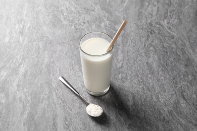 Photo of Delicious protein shake in glass and spoon with powder on grey table