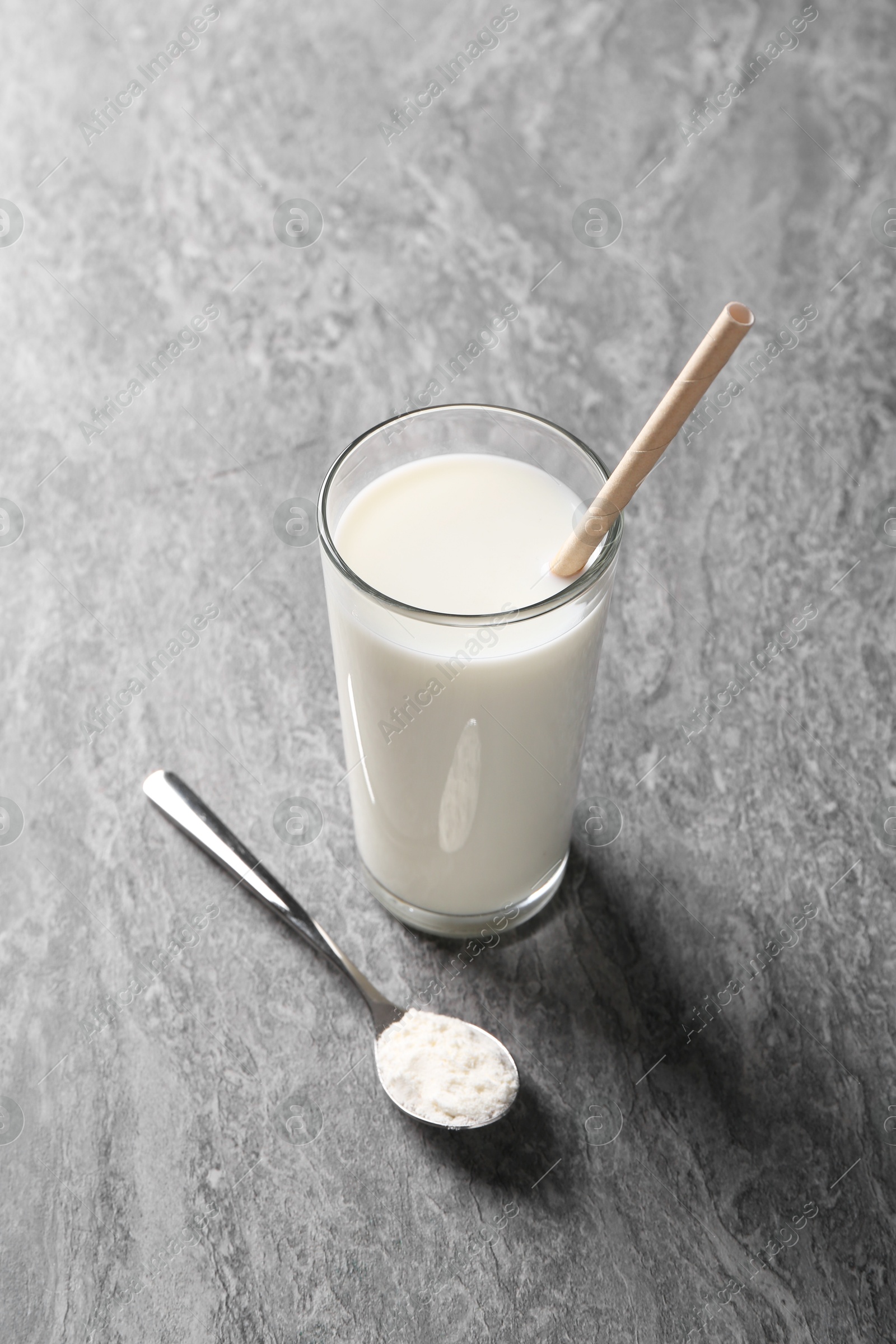 Photo of Delicious protein shake in glass and spoon with powder on grey table