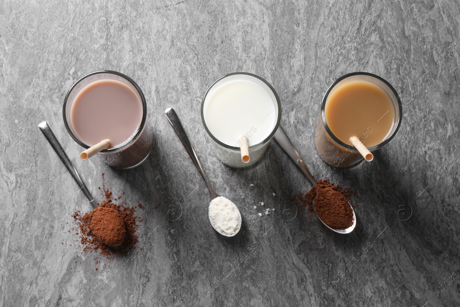 Photo of Delicious protein shakes in glasses and spoons with powder on grey table, flat lay