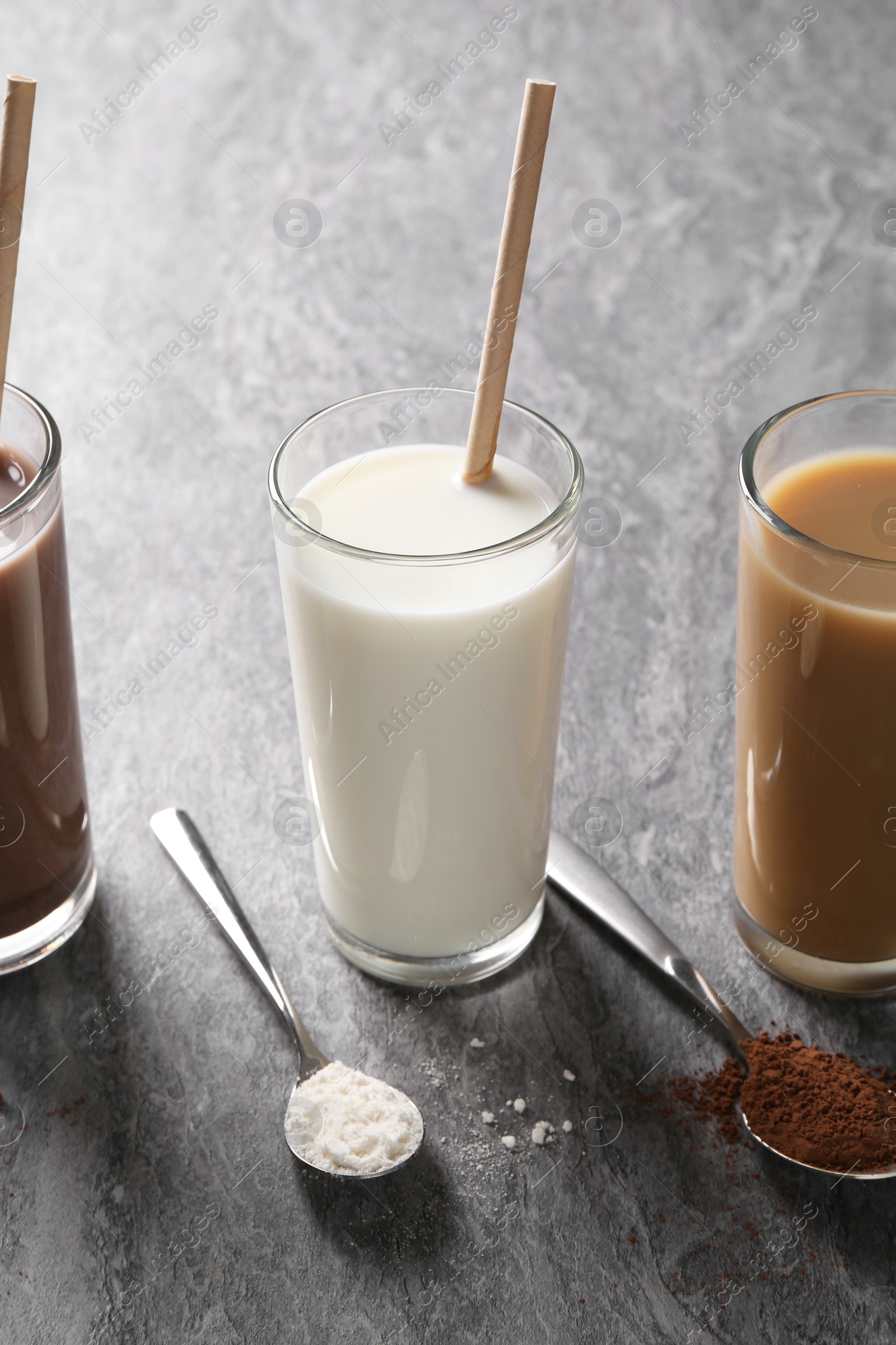 Photo of Delicious protein shakes in glasses and spoons with powder on grey table