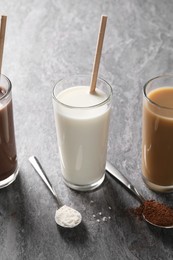 Photo of Delicious protein shakes in glasses and spoons with powder on grey table