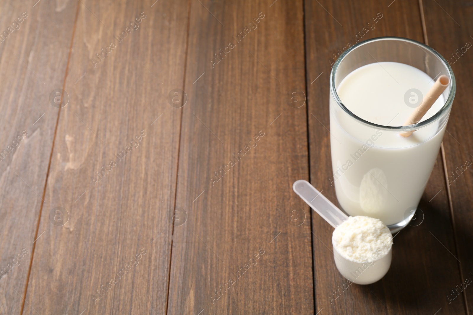 Photo of Delicious protein shake in glass and scoop with powder on wooden table, space for text