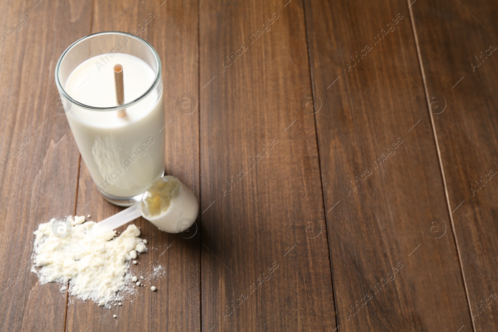 Photo of Delicious protein shake in glass, scoop and powder on wooden table, space for text