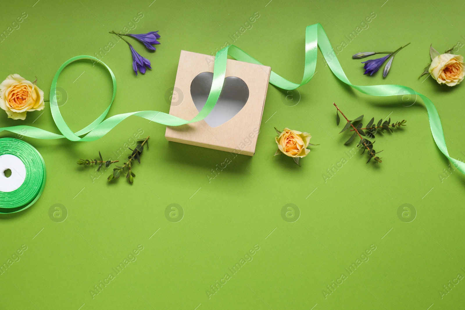 Photo of Flat lay composition with beautiful ribbon reel and gift box on green background, space for text