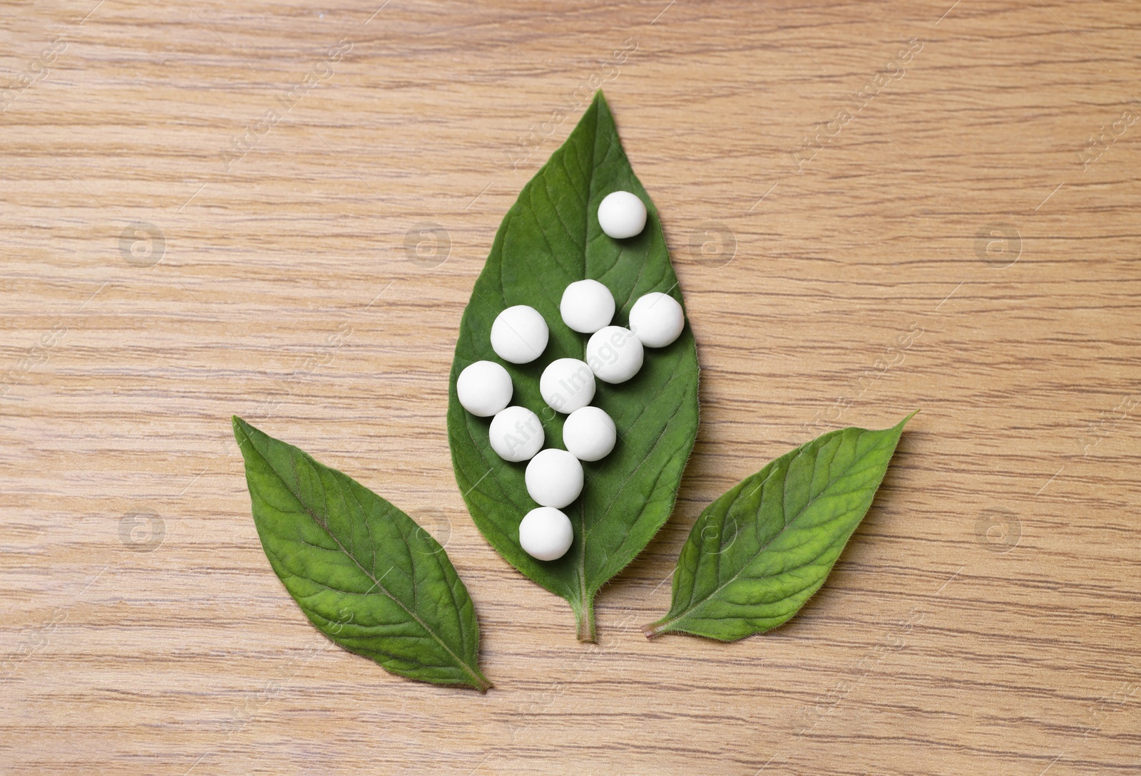 Photo of Homeopathy. Many pills and green leaves on wooden table, flat lay