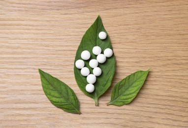 Photo of Homeopathy. Many pills and green leaves on wooden table, flat lay