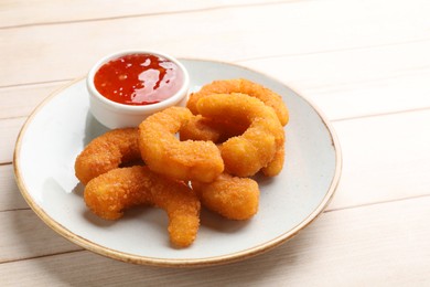 Photo of Tasty breaded fried shrimps and sauce on light wooden table