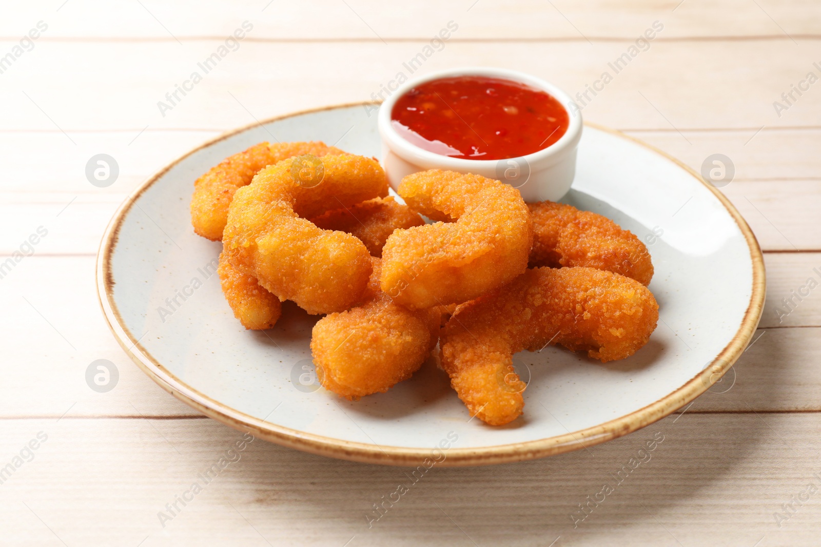 Photo of Tasty breaded fried shrimps and sauce on light wooden table